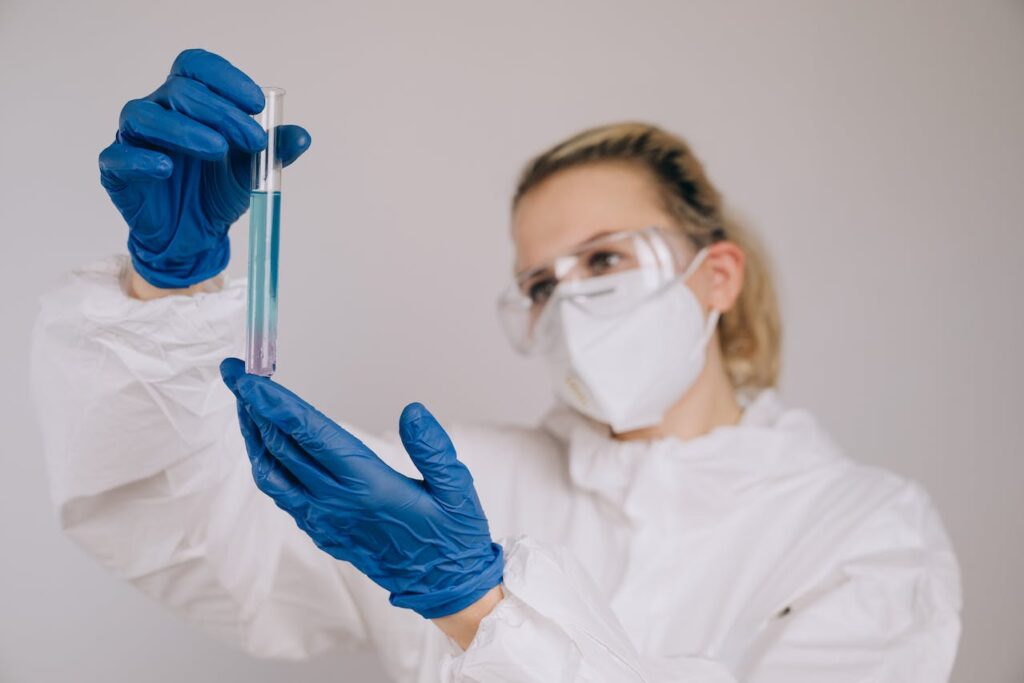 A female scientist in a lab coat and gloves carefully holds a test tube, conducting an experiment